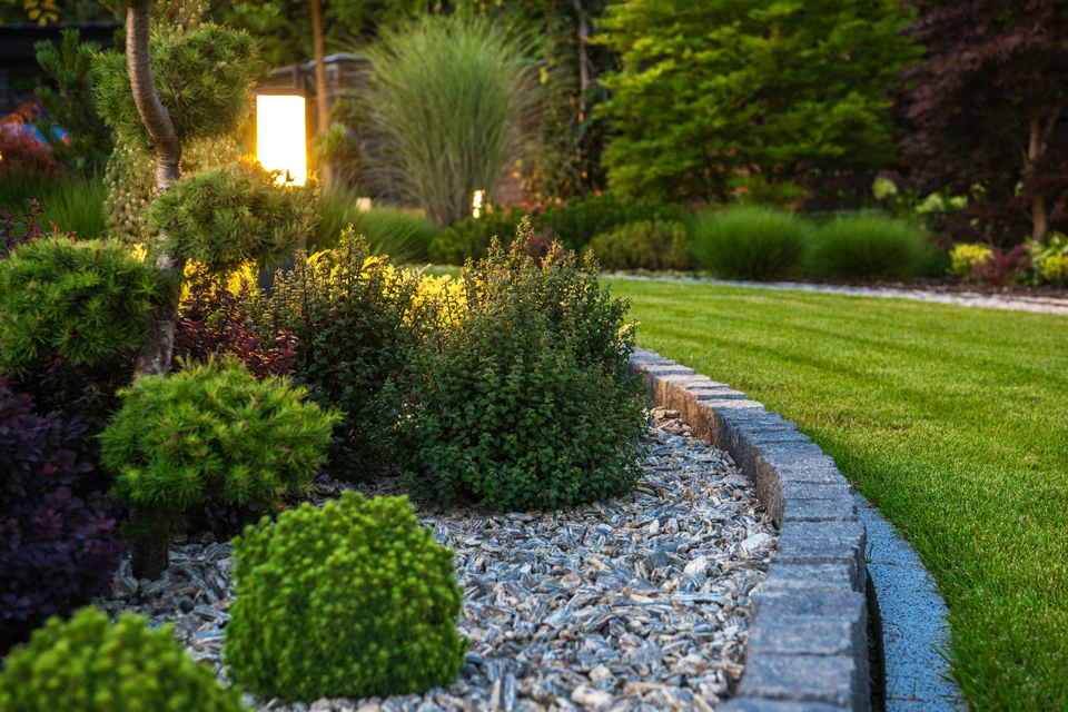 Jardin paysager avec massifs d'arbustes, bordure en pierre naturelle, paillis d'écorce et pelouse entretenue