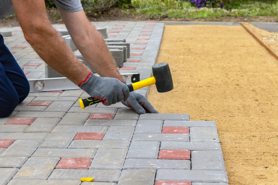 Chantier extérieur de pose de pavés autobloquants par un ouvrier équipé de gants de protection