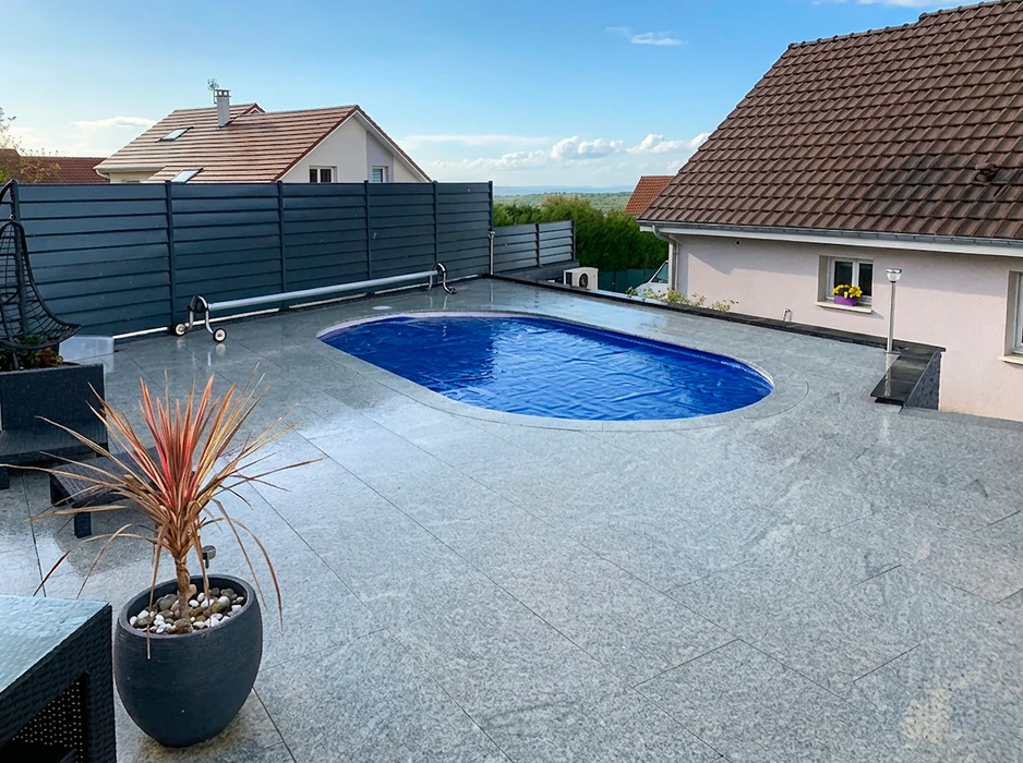 Piscine rectangulaire extérieure avec revêtement intérieur liner bleu clair, entourée d'une plage en dalles de granit gris flammé