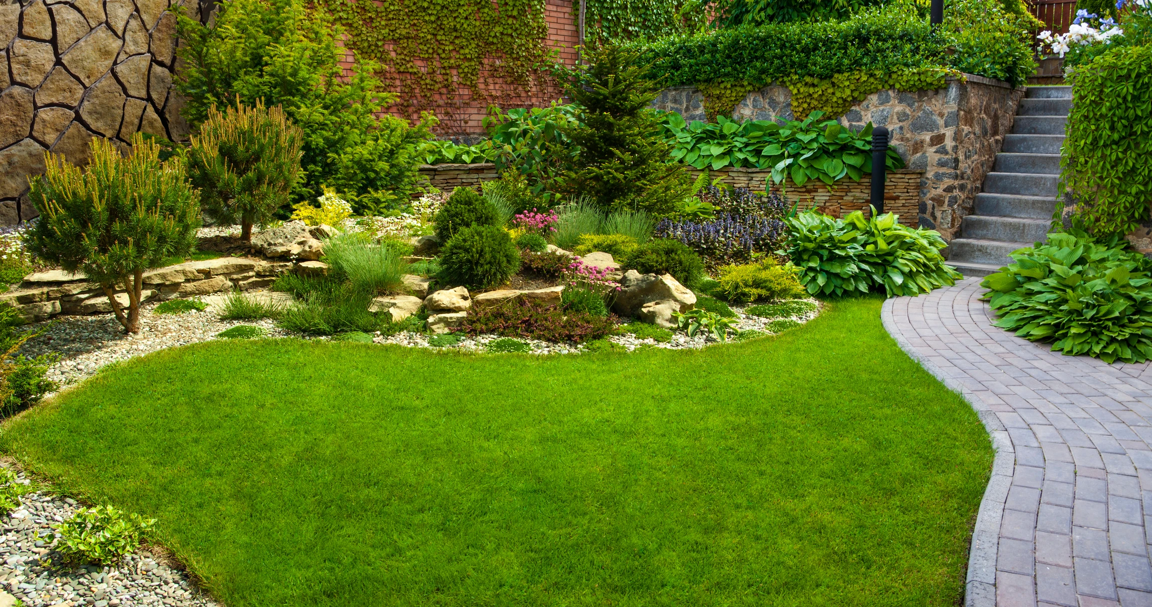 Jardin résidentiel paysagé avec pelouse verdoyante parfaitement entretenue, parterres de fleurs colorées incluant azalées roses, hostas et vivaces